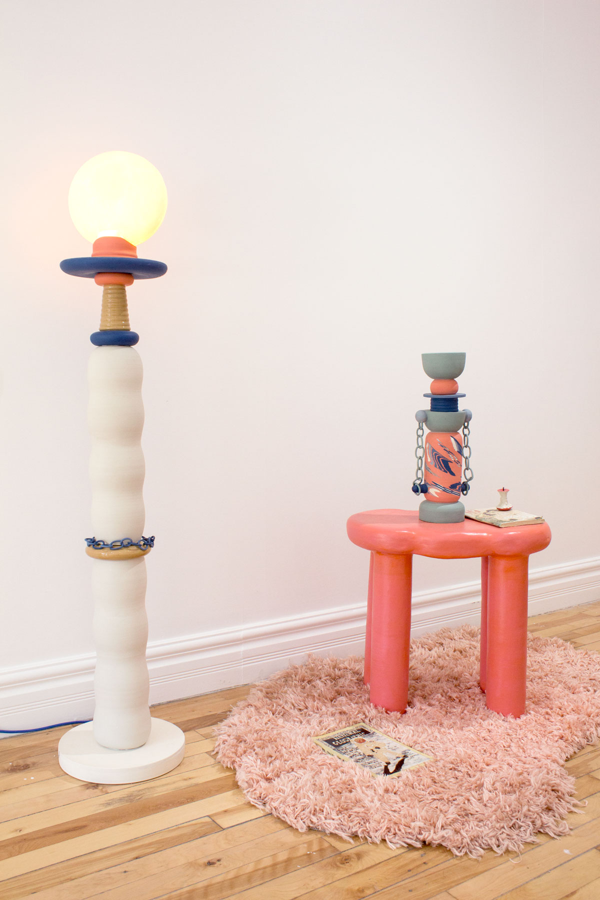 Tall ceramic lamp, pink ceramic table with rounded edges and a wacky multicolored vessel placed on top