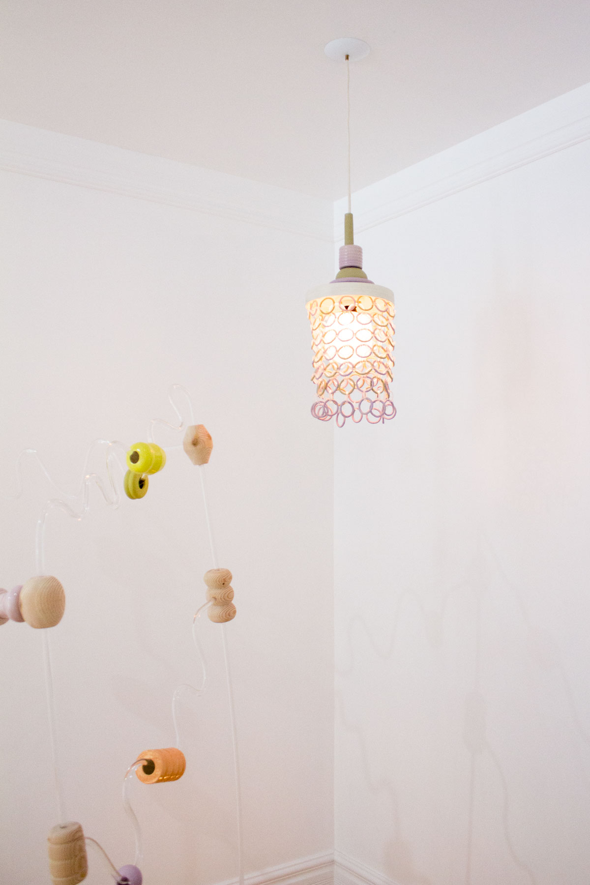 Ceramic and lucite chainmail lamp hanging above lucite structure with ceramic and wood beads